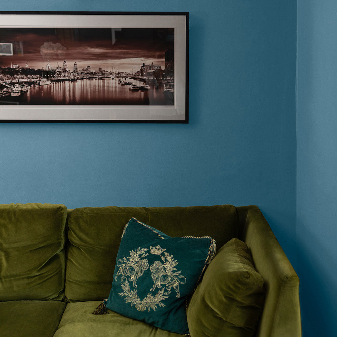 Corner of a living room decorated in Morning Dip, a blue slate paint from Zhoosh, paired with a green sofa.